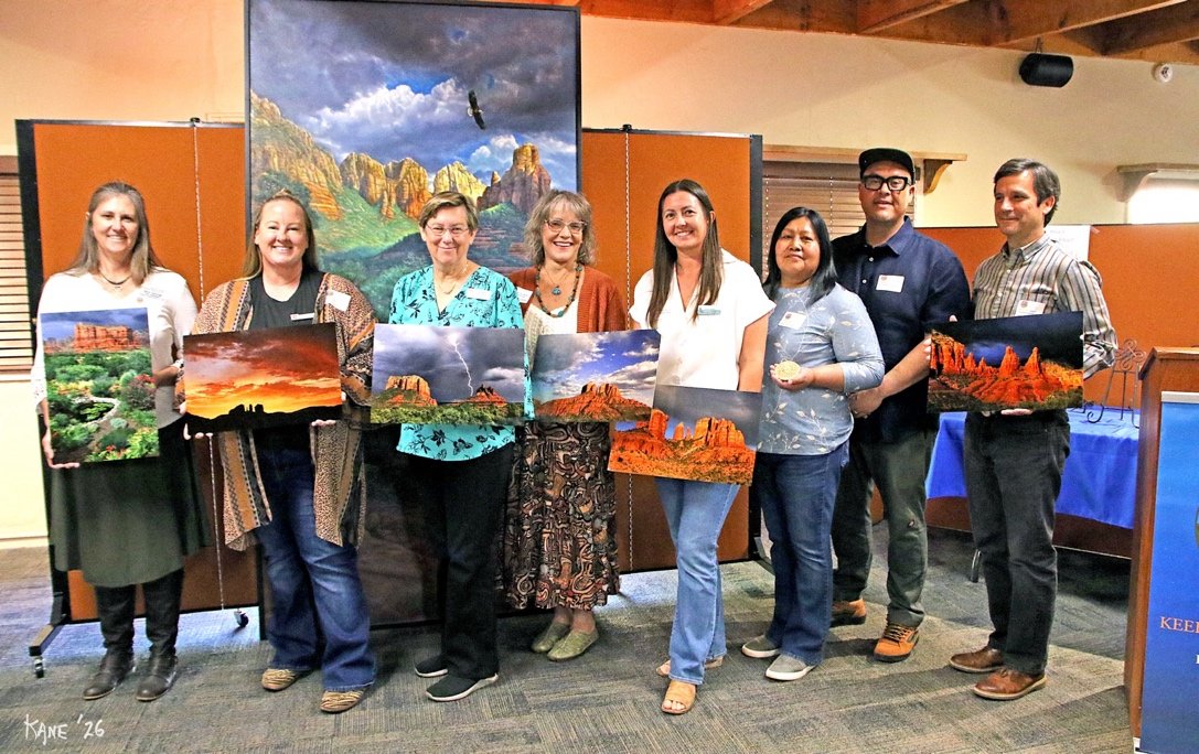 Eight 2026 Awards of Excellence honorees holding their framed awards in front of a landscape mural